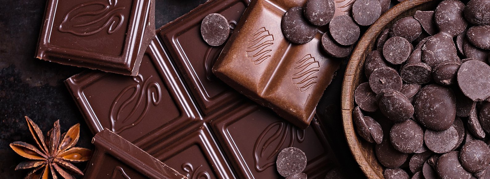 Dark chocolate bars, chocolate drops and cocoa on a dark table
