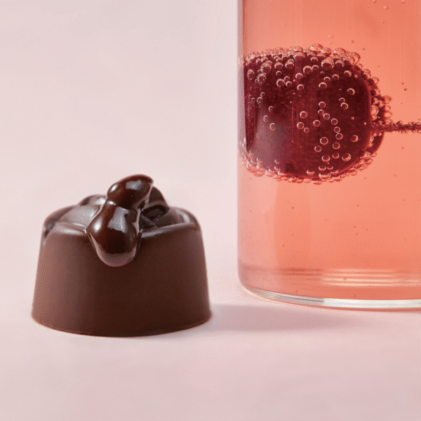 Filled chocolate praline with a glossy cherry topping beside a sparkling drink