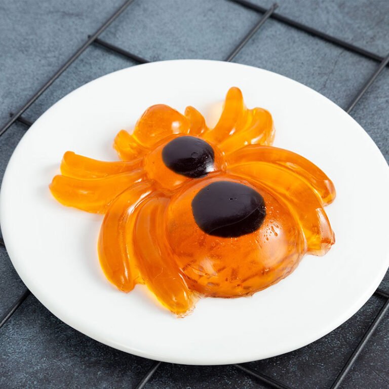 Large orange spider-shaped gummy candy on a white plate