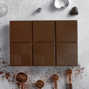 Milk chocolate baking block on a marble surface with cocoa powder in measuring spoons