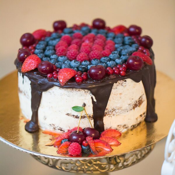 Berry-topped drip cake displayed on a gold cake drum